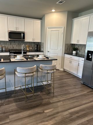 Modern kitchen with elegant white cabinetry, a sleek black countertop, and gold-accented barstools, creating a stylish space.