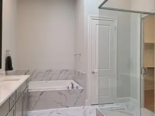A chic bathroom featuring a marble-tiled bathtub, sleek vanity, and a spacious glass shower enclosure.
