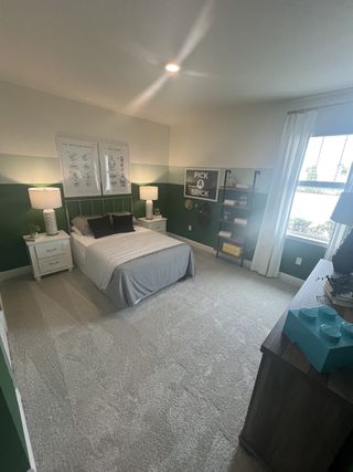 A cozy bedroom with green accent walls, plush carpeting, and natural light.
