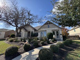 A charming stone home with elegant landscaping and mature trees in Oaks at San Gabriel by Brohn Homes (Georgetown, TX).