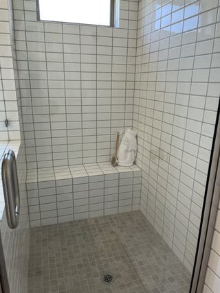 A sleek walk-in shower with white subway tiles, a built-in bench, and natural light peeking through a high window.
