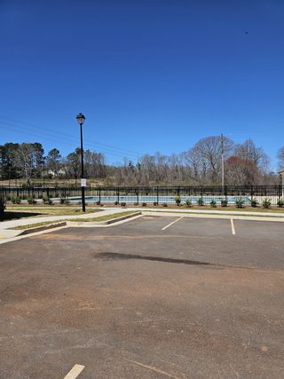 Community Amenities A sunny view of an empty parking lot with a community pool enclosed by a black fence in Ponderosa Farms by Chafin Communities in Gainesville, GA.