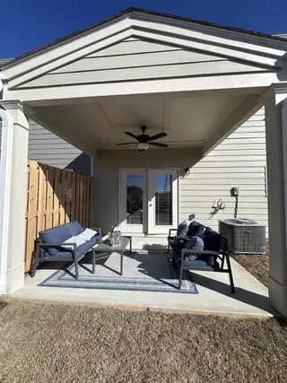 A cozy covered patio with seating, outdoor fan, and rug in a stylish design.