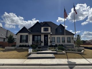 A stunning white brick home with dark shutters and a manicured lawn in Broken Oak by Highland Homes (Georgetown, TX).