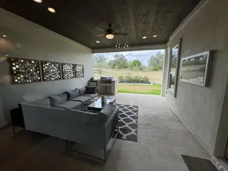 A cozy enclosed patio with modern seating, stylish wall art, a barbecue grill, and scenic views of the backyard.
