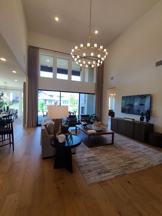Model Home A spacious living area with high ceilings, a grand chandelier, modern furniture, and a large window for ample natural light.