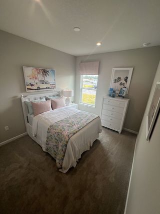 Model Home A cozy bedroom with soft carpeting, pastel bedding, and vibrant beach-themed artwork on the walls.