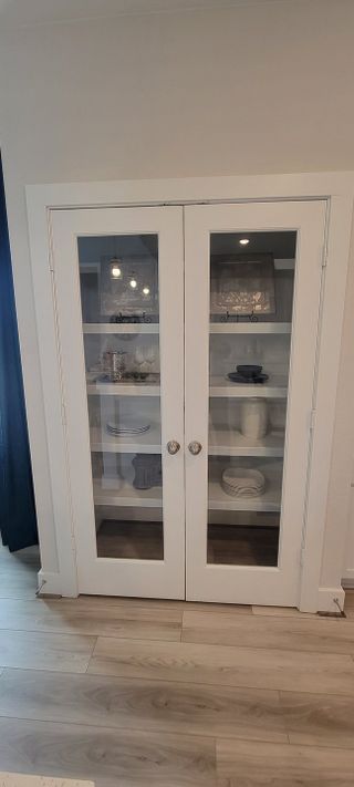 Model Home A chic glass-paneled cabinet with elegant tableware and decor on display, set against light wood flooring.