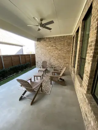 A cozy covered patio with brick walls, comfortable seating, and a ceiling fan for relaxing outdoors.