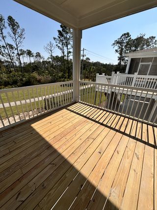 A spacious wooden deck with white railing, offering a serene view of tall trees under a clear blue sky.