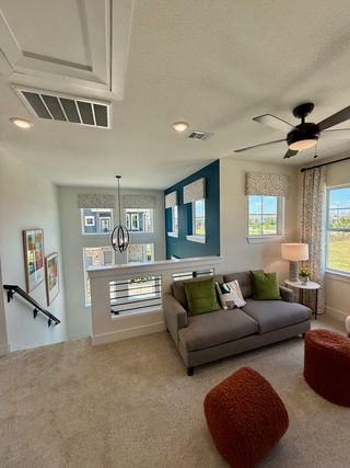 Model Home Bright loft area with cozy gray sofa, colorful pillows, modern ceiling fan, and natural light from multiple windows.