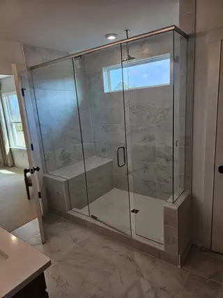 A spacious luxury shower with marble tiles, glass doors, and a built-in bench, perfect for a modern bathroom.