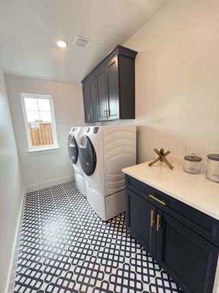 A chic laundry room featuring geometric patterned tiles, dark cabinetry, and modern appliances.