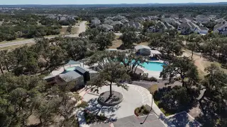 An aerial shot of the Caliterra community by Drees Custom Homes in Dripping Springs, TX, featuring a community pool area surrounded by lush trees and residential homes.