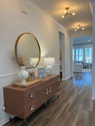 Model Home A modern hallway with elegant wood flooring, a chic console, round mirror, and soft lighting leading to a cozy living area.