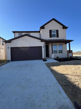 A modern stone and brick home with a covered porch and dark trim accents in Princeton Estates by KB Home (Princeton, TX).