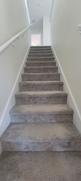A staircase in The Granary home, featuring gray carpeting, white walls, and a white handrail leading to the upper level (San Antonio, TX).