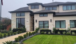 A striking modern stone home with sleek black windows and lush landscaping in Weston Oaks by Perry Homes (San Antonio, TX).