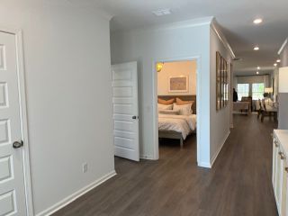 A modern hallway with sleek wood flooring leads to a cozy bedroom and a bright, open-plan living area.