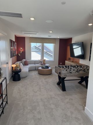 A cozy rec room with a curved sofa, foosball table, and mounted TV, perfect for relaxation and entertainment.