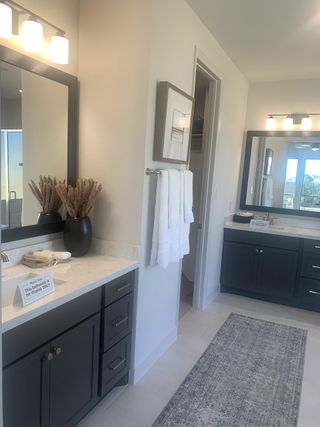 Model Home A modern bathroom featuring dual dark vanities, elegant lighting, and a decorative runner rug.