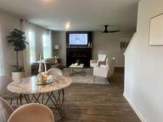Modern living room with a marble dining table, cozy seating, wood floors, and a stylish fireplace with a mounted TV.