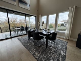 A chic dining area with a sleek black table, modern chairs, large windows, and a view to an inviting patio deck.