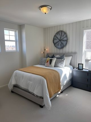 A cozy bedroom featuring a plush bed with layered pillows, a warm throw, and soft lighting, complemented by natural light.