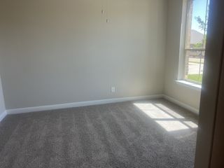 Model Home A sunlit carpeted room with neutral walls and a large window offers warmth and comfort.