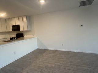 A modern kitchen with sleek white cabinets, stainless steel appliances, and a spacious open layout featuring wood-style flooring.