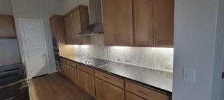Model Home A sleek kitchen with spacious wooden cabinets, a stylish backsplash, and glossy countertops illuminated by under-cabinet lighting.