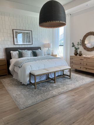Model Home A stylish bedroom with textured walls, cozy bedding, and a contemporary pendant light on a soft rug with wood floors.