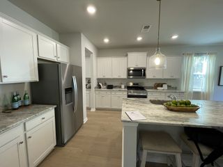 A modern kitchen with sleek stainless steel appliances, white cabinetry, a large island, and elegant pendant lighting.