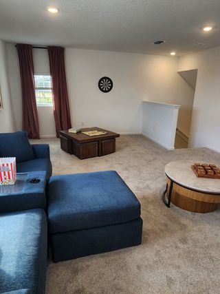 A cozy living area with plush blue seating, neutral carpet, and a dartboard.