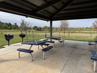 A serene picnic area with blue tables, grills, and a scenic view in Bryson by Highland Homes (Leander, TX).