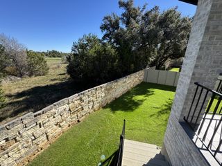 A serene backyard with lush grass and stone fencing in Wolf Ranch - 55' by Westin Homes (Georgetown, TX).