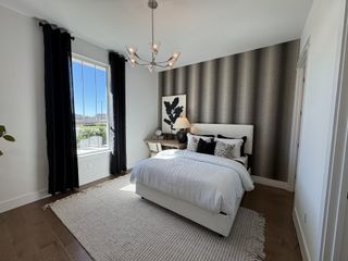 Model Home A cozy bedroom with a chic accent wall, elegant chandelier, large window with black drapes, and plush bedding on a neutral rug.