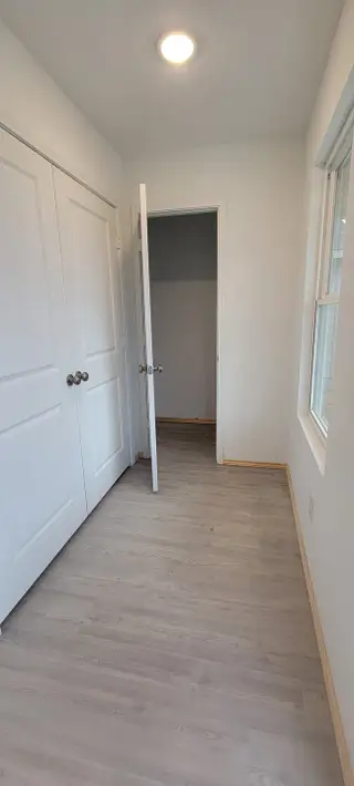 A bright room with light wood flooring, white doors, and a window, offering a minimalist aesthetic and natural lighting.