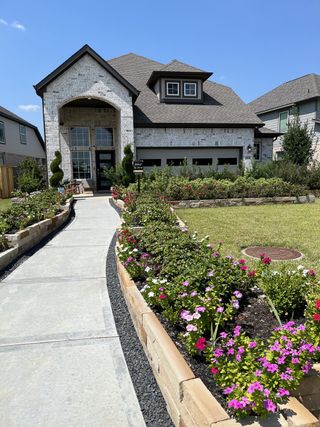 A beautiful brick home with manicured gardens and a curved walkway in Dellrose by Chesmar Homes (Hockley, TX).