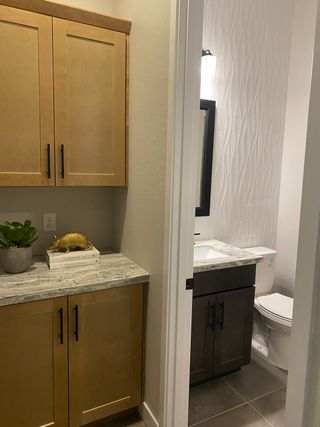 A stylish powder room features a dark wood vanity with a white countertop, textured white tile backsplash, and a light wood cabinet with a gray countertop.