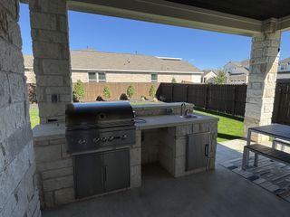 A beautifully designed outdoor kitchen with a built-in stainless steel grill, stone countertops, and a covered patio for perfect outdoor gatherings.