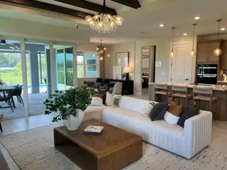 A spacious living area features a modern sectional, chic lighting, and an open view to a poolside patio, perfect for relaxation.
