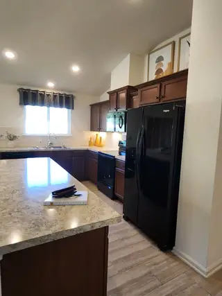 Model Home A cozy kitchen with rich wood cabinetry, black appliances, and marble-look countertops.