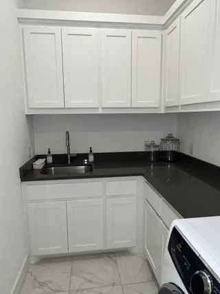A spacious laundry area with white cabinetry, black countertops, and a stainless steel sink, providing ample storage and functionality.