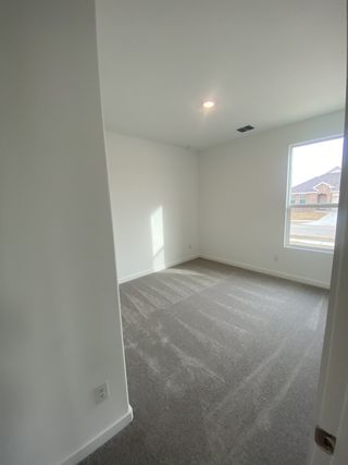 A bright, carpeted room with natural light filtering in through a large window, featuring clean, white walls.