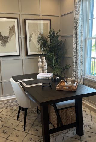 A chic home office with a black desk, neutral decor, and natural light, enhanced by stylish wall art and a patterned rug.