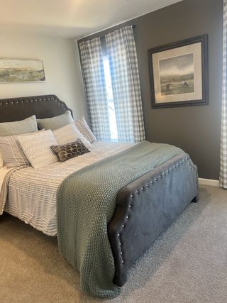 A cozy bedroom with a studded headboard, patterned bed linens, and plaid curtains, creating a serene, stylish retreat.