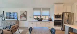 Bright kitchen with white cabinets, gold hardware, and stainless steel appliances, flowing into a cozy dining area.