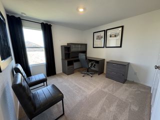 A modern home office with a sleek dark desk, plush chairs, and framed art on white walls.