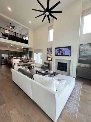 A spacious living room with vaulted ceilings, contemporary fans, a cozy fireplace, and elegant kitchen views.